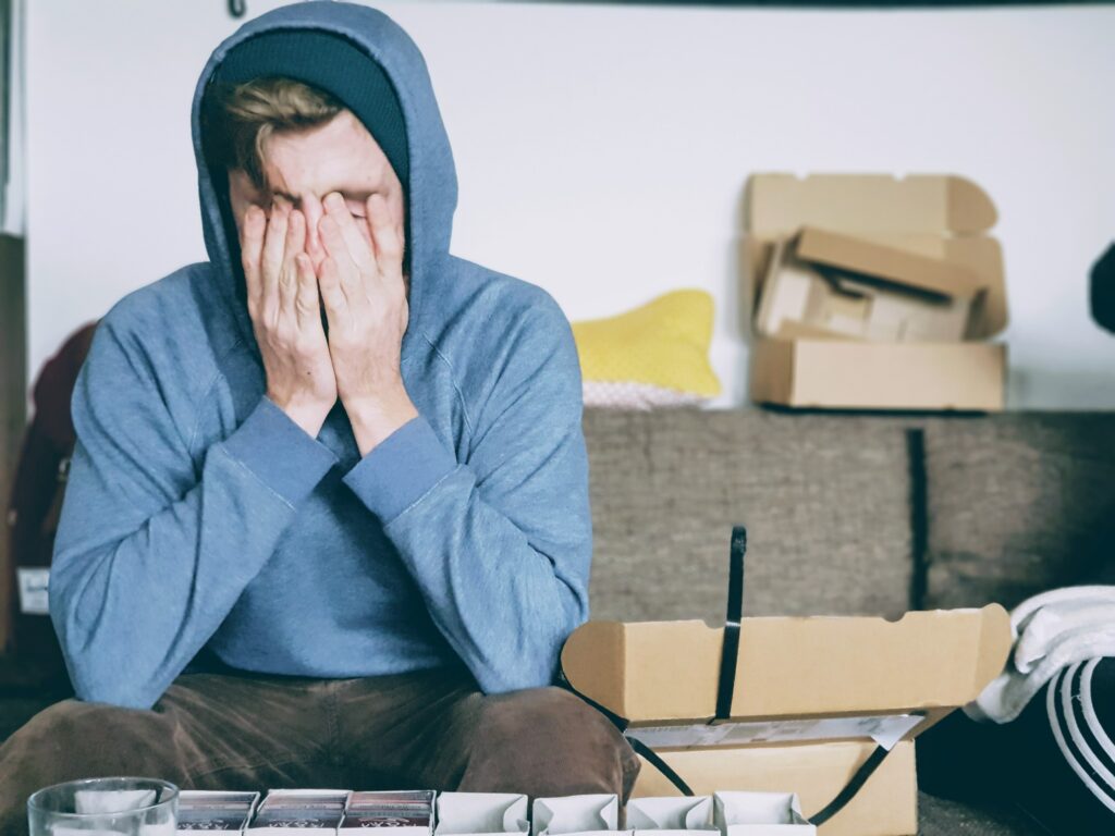 Junger Mann sitzt auf der Couch und hält erschöpft seinen Kopf in den Händen: Auswirkungen von Mobbing am Arbeitsplatz